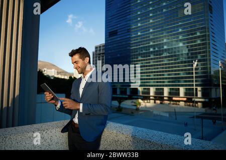 Smiling businessman standing on an office terrace using a tablet Stock Photo