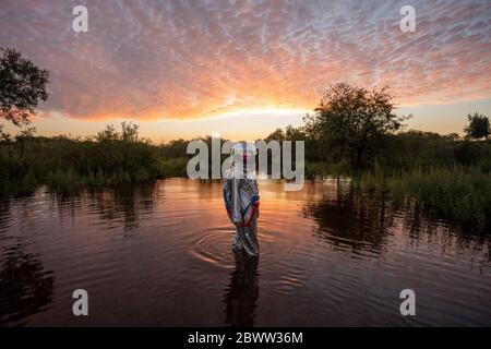 Spacewoman walking in water at sunset Stock Photo