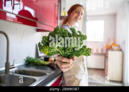 Young woman standing in kitchen, holding cale Stock Photo