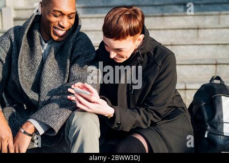 Happy young couple in the city sitting on stairs using cell phone Stock Photo