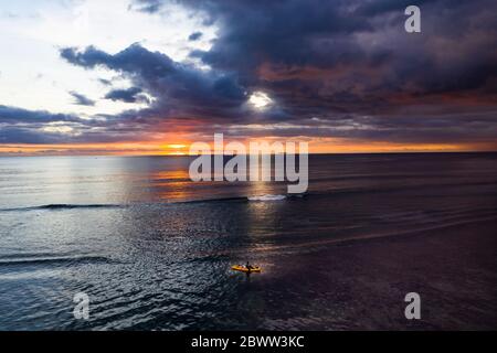 Mauritius, Helicopter view of dark storm clouds over lone surfer paddleboarding in Indian Ocean at sunset Stock Photo