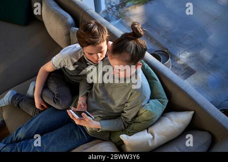 Brother and sister sitting on couch at home using smartphone Stock Photo