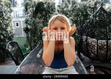 Portrait of blond girl sitting on terrace pulling funny faces Stock Photo