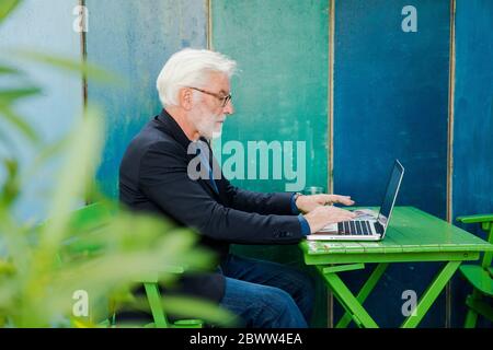 Senior man sitting at table outdoors using laptop Stock Photo