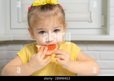 little girl in a yellow blouse eats grapefruit Stock Photo