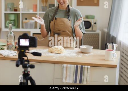 Young woman wearing apron standing at the kitchen and making dough for cake and shooting the video for content Stock Photo