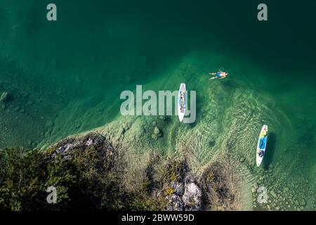 Germany, Bavaria, Aerial view of two paddleboarders relaxing on green shore of Lake Walchen Stock Photo