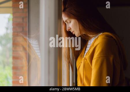 Redheaded woman with eyes closed leaning against window