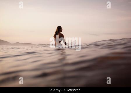 Female surfer sitting on surfboard in the evening, Costa Rica Stock Photo