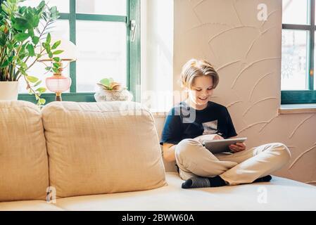 Boy sitting on couch in living room at home using tablet Stock Photo