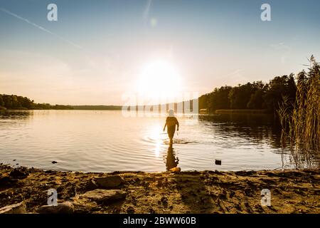 Boy walking in lake against sky during sunset, Strausberg, Germany Stock Photo