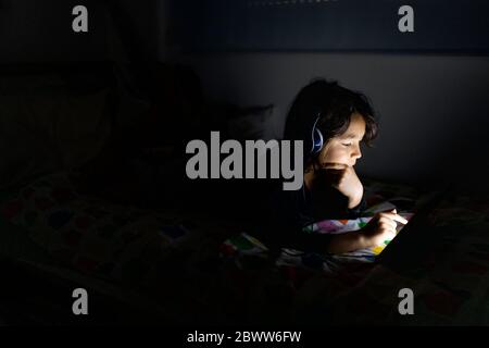 Boy lying on bed at home using headphones and digital tablet Stock Photo