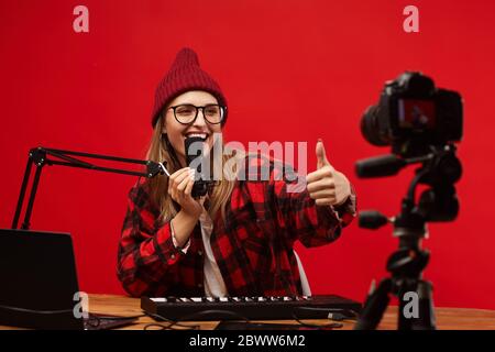 Young smiling woman in eyeglasses showing thumb up to the camera and singing she shooting the content Stock Photo