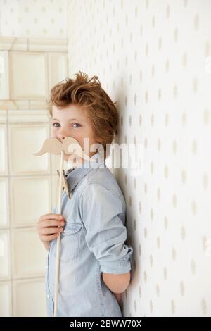 Portrait of boy holding cardboard moustache Stock Photo