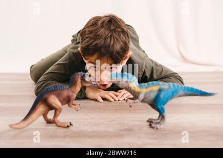 Portrait of little boy crouching on the floor playing with toy dinosaurs