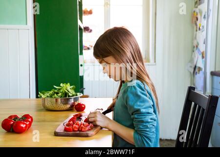 Girl cutting tomatoes on chopping board in kitchen Stock Photo