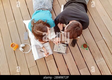 Teenage couple lying on terrace learning together with digital tablet Stock Photo