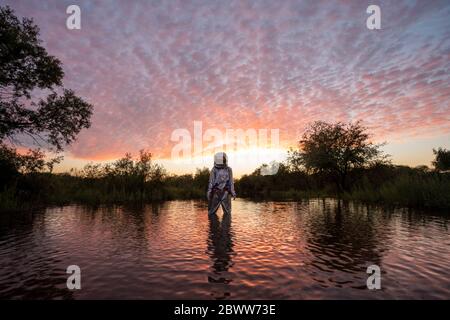 Spacewoman standing in water at sunset Stock Photo