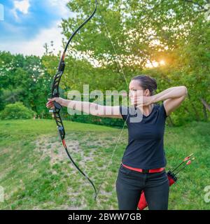 competition in archery in nature. A young attractive woman points an arrow at a target Stock Photo