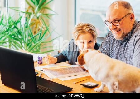 Father helping son doing homework with dog on desk Stock Photo