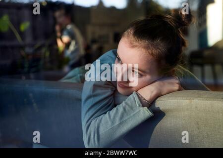 Girl on couch at home looking out of window Stock Photo