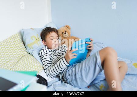 Boy lying in bed using digital tablet Stock Photo