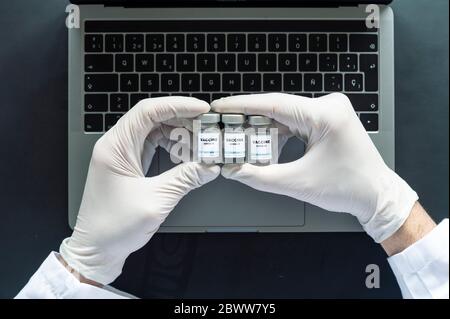 Directly above shot of doctor holding vaccine medical vials over laptop at laboratory desk Stock Photo