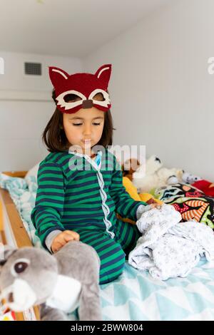 Portrait of little girl with fox mask crouching on bunk bed at home Stock Photo