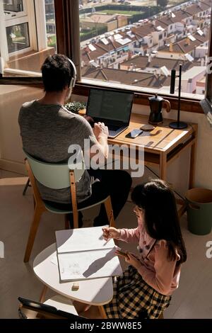 Father working on laptop while his daughter doing homework Stock Photo