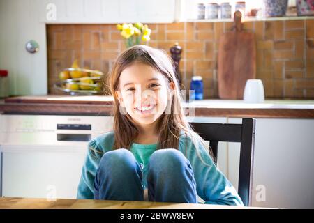 Smiling girl sitting at kitchen table and looking at camera Stock Photo