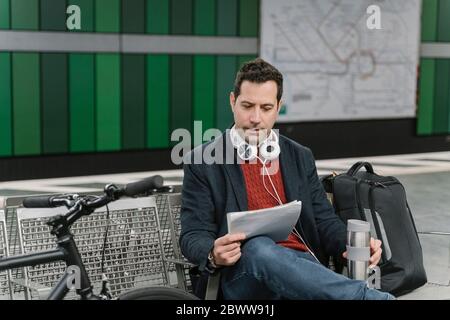 Businessman with bicycle reading documents while sitting at subway station platform, Frankfurt, Germany Stock Photo