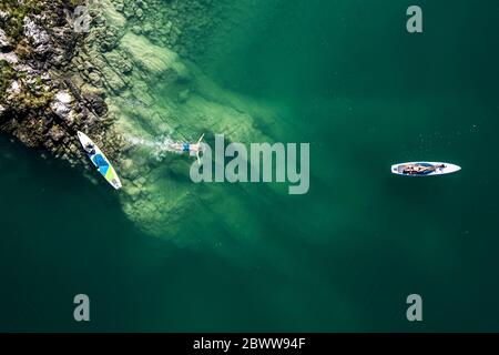 Germany, Bavaria, Aerial view of two paddleboarders relaxing on green shore of Lake Walchen Stock Photo