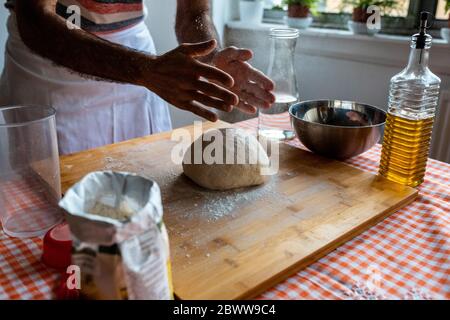 Crop view of man spreading flour on dough ball in the kitchen