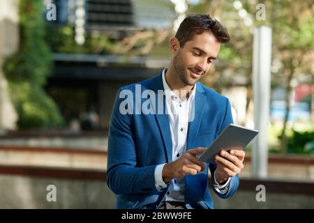 Smiling young businessman standing outside using a digital tablet Stock Photo