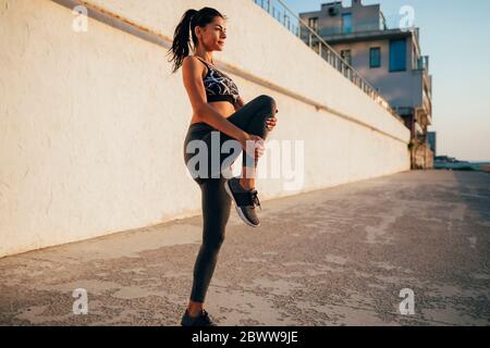 Full length of young female athlete stretching on promenade during sunny day Stock Photo