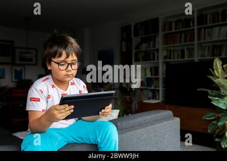 Portrait of boy sitting on backrest of couch looking at digital tablet Stock Photo