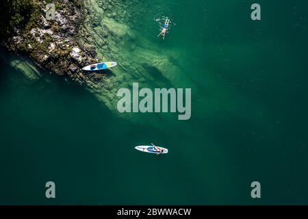 Germany, Bavaria, Aerial view of two paddleboarders relaxing on green shore of Lake Walchen Stock Photo