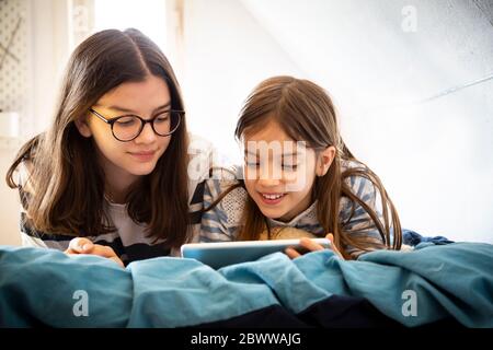 Sisters using tablet lying on bed Stock Photo