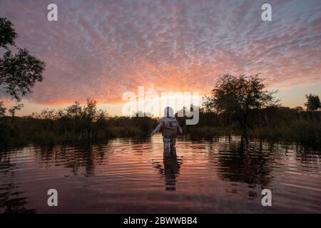 Spacewoman walking in water at sunset Stock Photo
