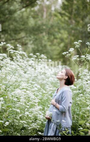 Pregnant woman with hands on stomach relaxing amidst flowers in park Stock Photo