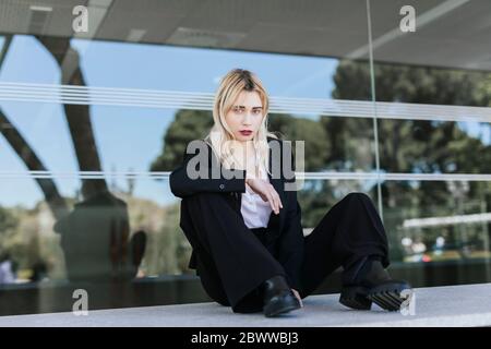 Portrait of young businesswoman with dyed blond hair sitting in front of office building Stock Photo
