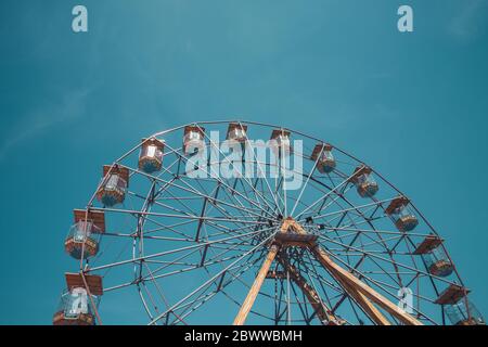 A distant view of a the top half of a symmetrical, vintage Ferris Wheel at a seaside fairground with copy space and blue sky background Stock Photo