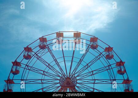 A distant view of a the top half of a symmetrical, vintage Ferris Wheel at a seaside fairground with copy space and blue sky background Stock Photo