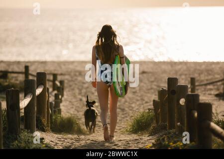Back view of young woman with surfboard walking to the beach in the evening, Almeria, Spain Stock Photo