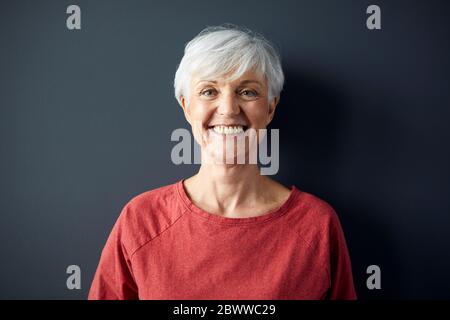 Portrait of happy senior woman wearing red shirt in front of grey wall Stock Photo