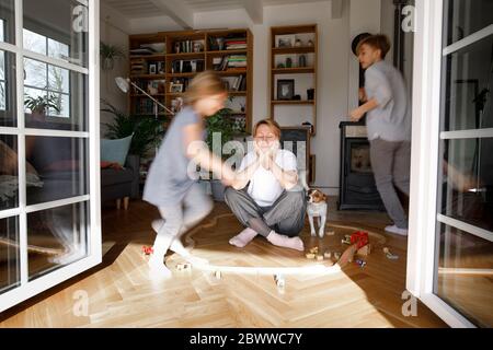 Stressed out mother sitting in the middle of toys, while children are running around her Stock Photo