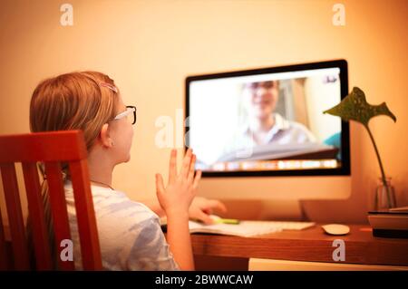 Back view of anonymous girl raising arm while sitting at desk and attending online lesson at home Stock Photo