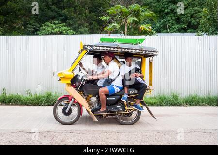 The famous filipino tricycle or tuk tuk (sometimes called rickshaw) makes its way along the busy main road going into Coron Town Proper. Coron Island. Stock Photo