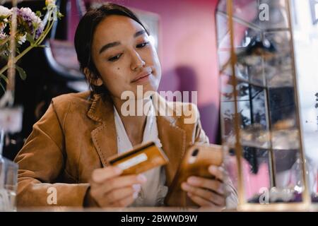 Thoughtful woman looking at smart phone and credit card in thrift store Stock Photo
