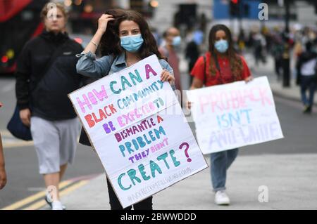 A woman holds a banner during a Black Lives Matter protest rally as it passes near to Victoria station, London, in memory of George Floyd who was killed on May 25 while in police custody in the US city of Minneapolis. Stock Photo